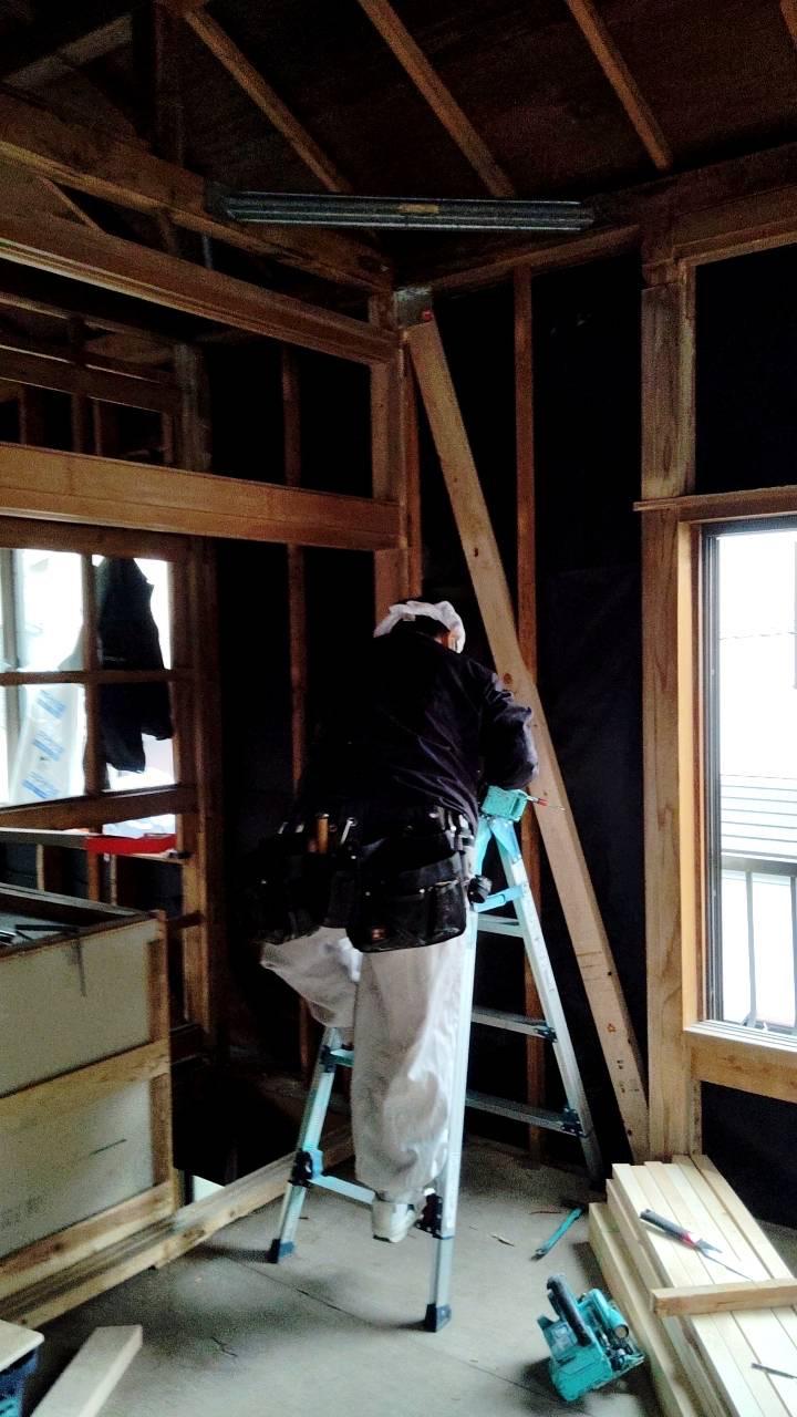 The frame exposed during seismic work — carpenter working at height on the structural posts and beams